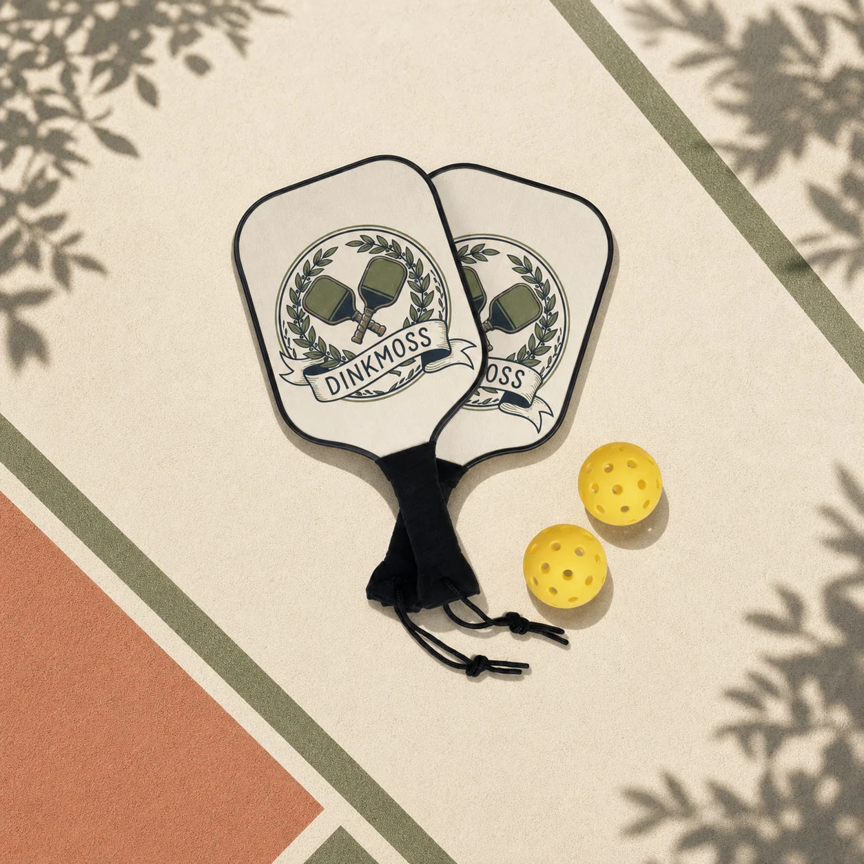 Two DINKMOSS pickleball paddles and two outdoor balls on a sunlit court